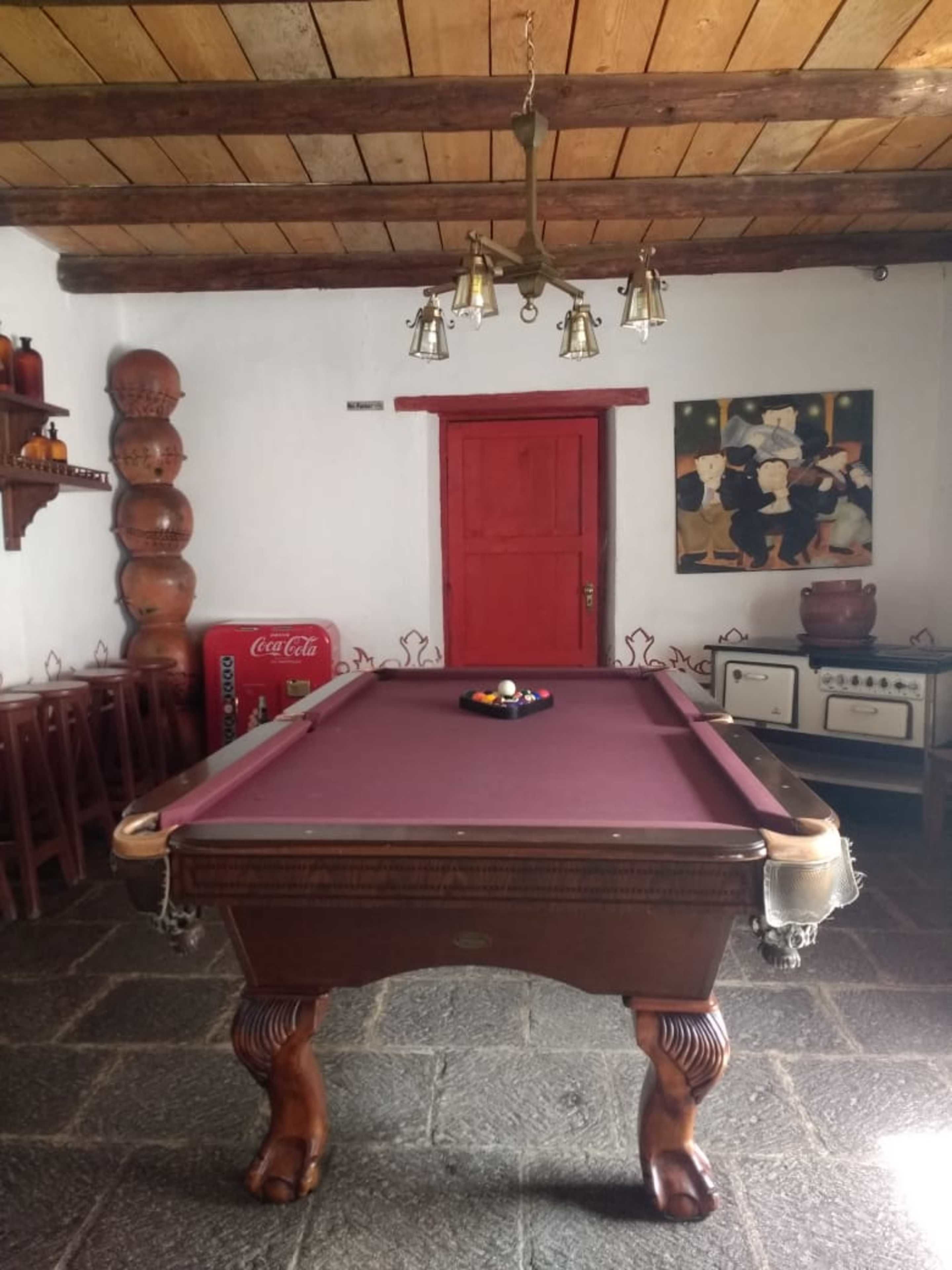 A pool table in a room with a red door, wooden ceiling beams, and a painting on the wall.