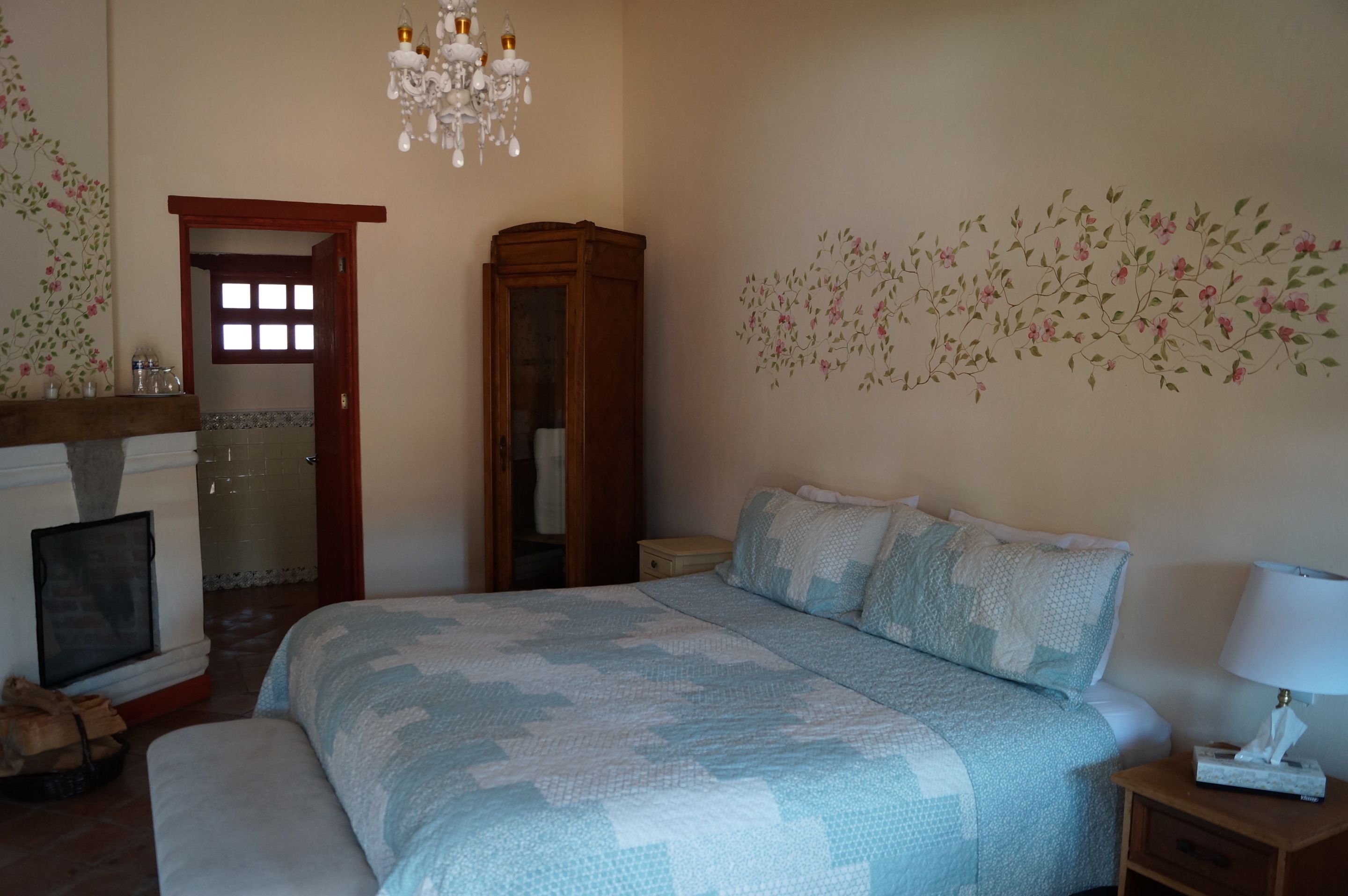 A bedroom with a large bed, a wooden wardrobe, a chandelier, and floral wall art.