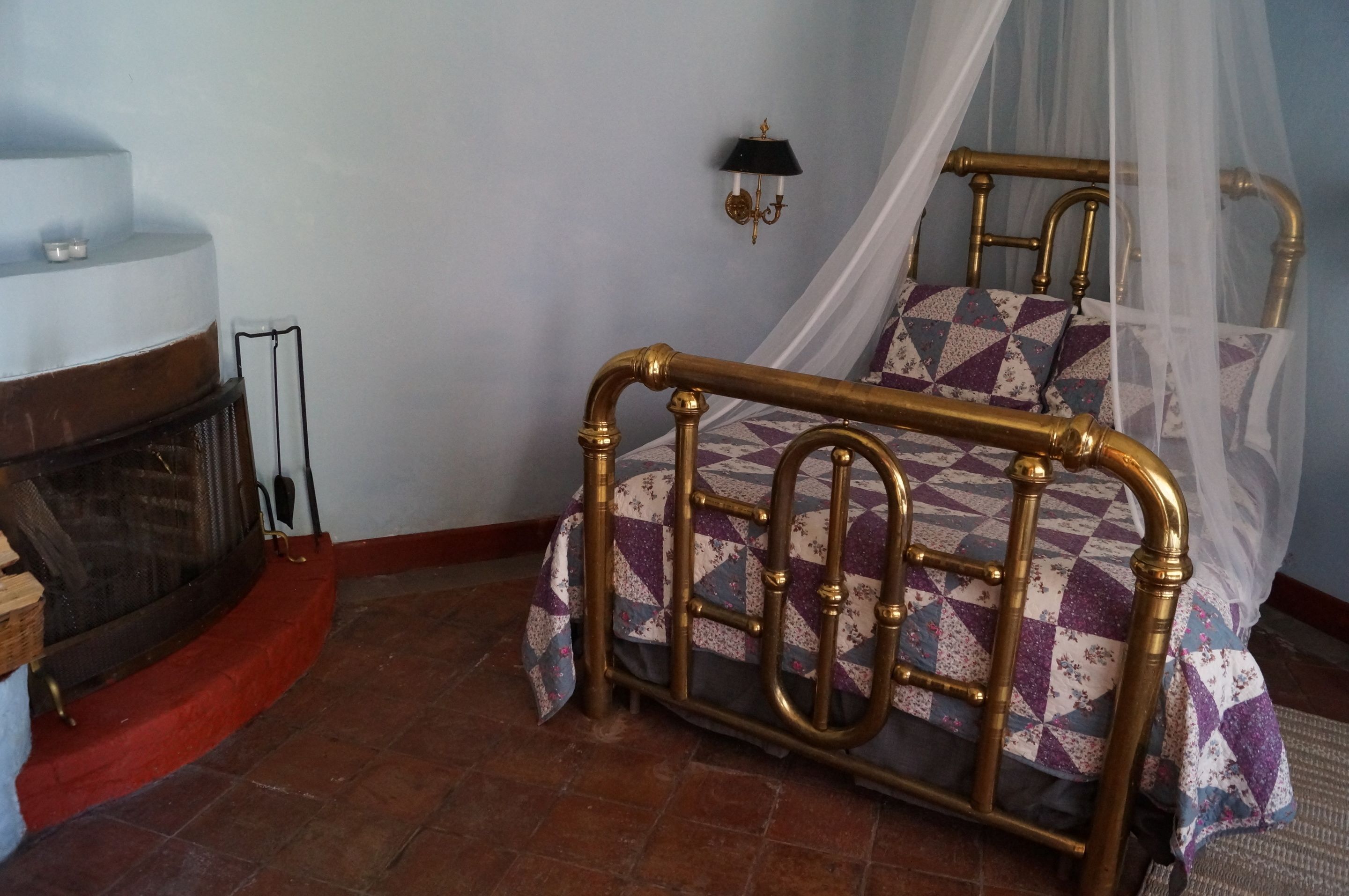 A bedroom with a four-poster bed, a fireplace, and a wall-mounted lamp.