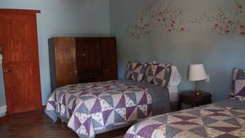 Un dormitorio con dos camas, un armario de madera, una mesita de noche con lámpara y decoración floral en la pared.