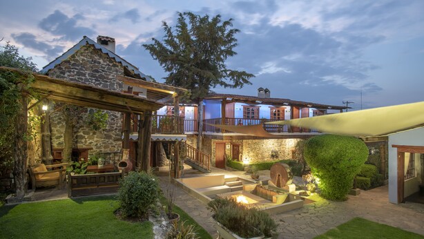 A stone building with a wooden pergola, outdoor seating, and a well-maintained garden.