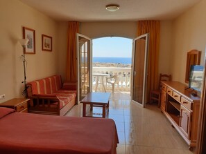 A hotel room with a bed, a sofa, a desk, a TV, and a balcony with a view of the sea. - Carolina Park (Costa del Silencio)
