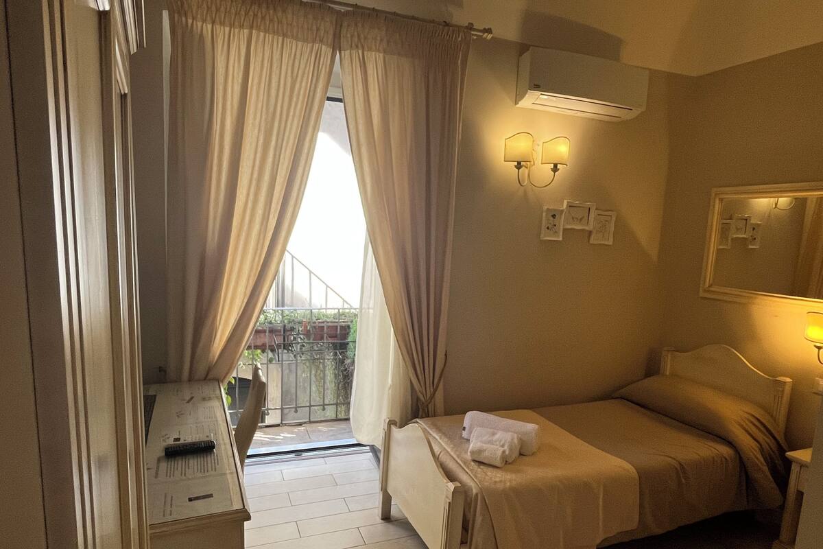 A hotel room with a bed, a bedside table, a mirror, and a window with curtains.