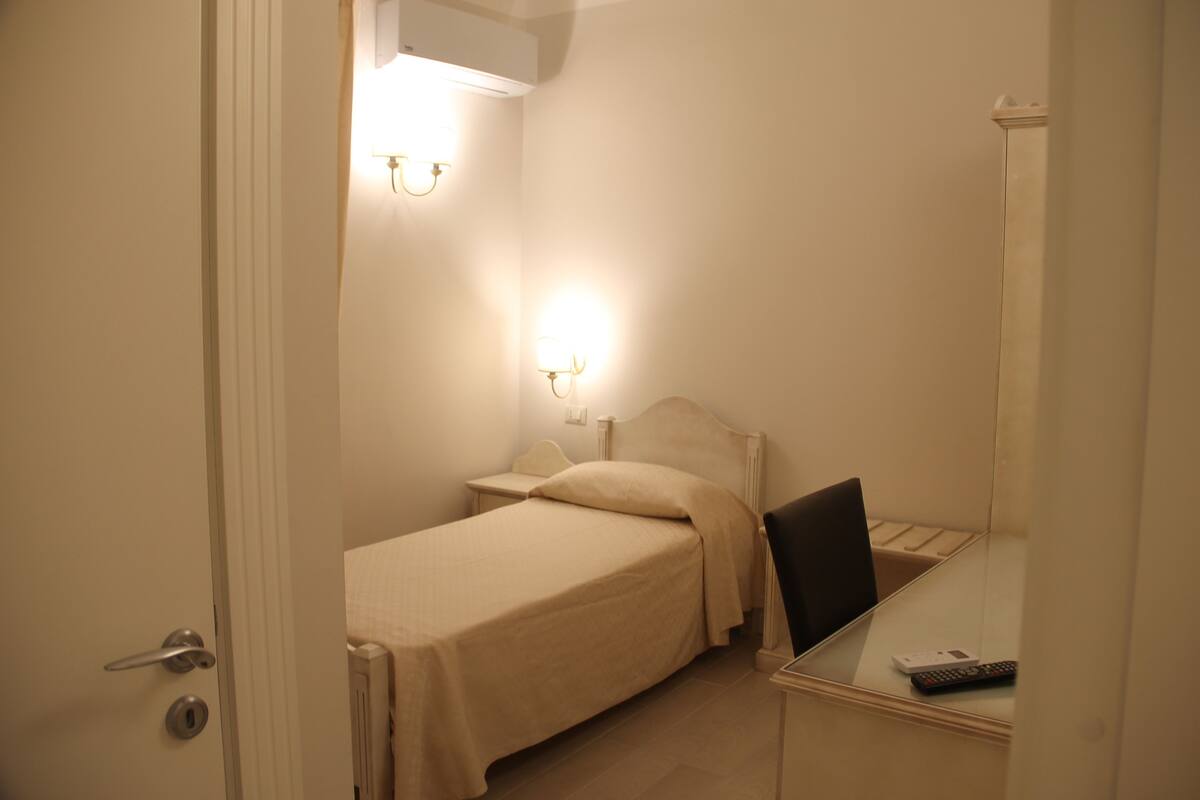 A small, neatly arranged bedroom with a single bed, bedside table, and a chair.