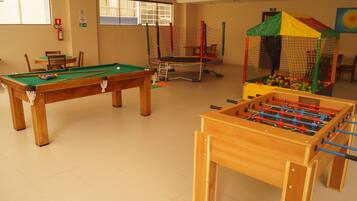A recreational room with a pool table, foosball table, and a play area with a colorful playhouse.