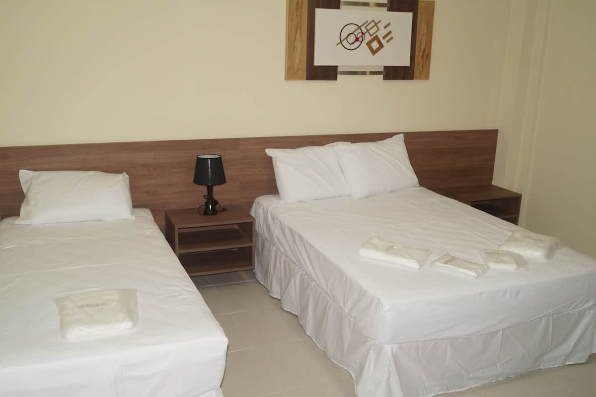 A hotel room with two single beds, each with white linens and pillows, a wooden headboard, a bedside table with a lamp, and a framed artwork on the wall.