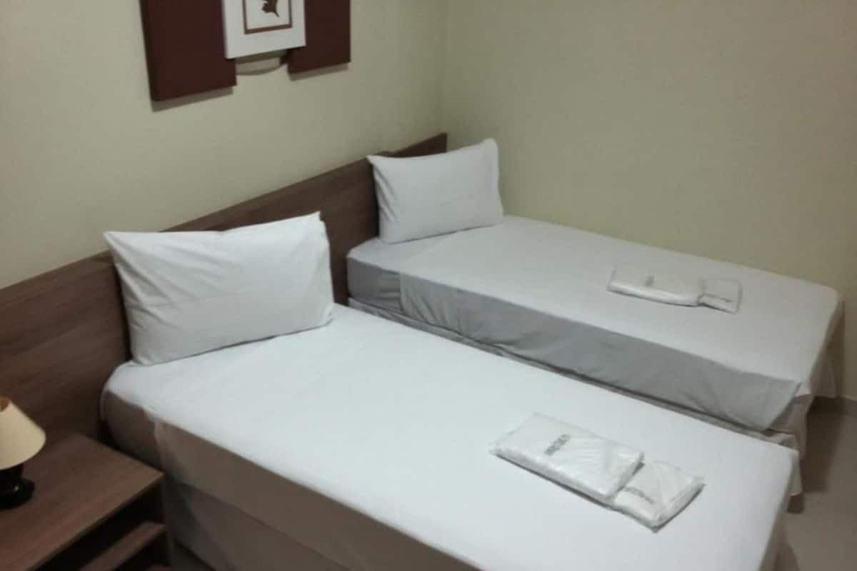 A double bed with white linens and a bedside table with a lamp.