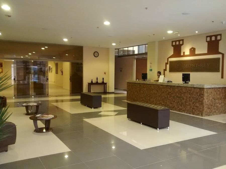 A hotel lobby with a reception desk, seating areas, and a clock on the wall.