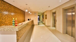 A hotel lobby with a reception desk, a clock, and elevators.