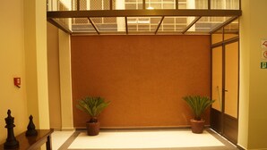 A hallway with two potted plants, a fire alarm, and a chessboard.