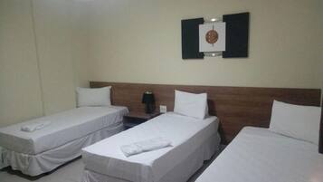 Habitación de hotel con tres camas individuales, un cabecero de madera, un reloj en la pared y una mesita de noche con lámpara.