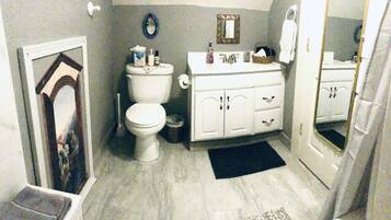 A bathroom with a toilet, sink, and mirror. There is a picture frame on the wall and a rug on the floor.