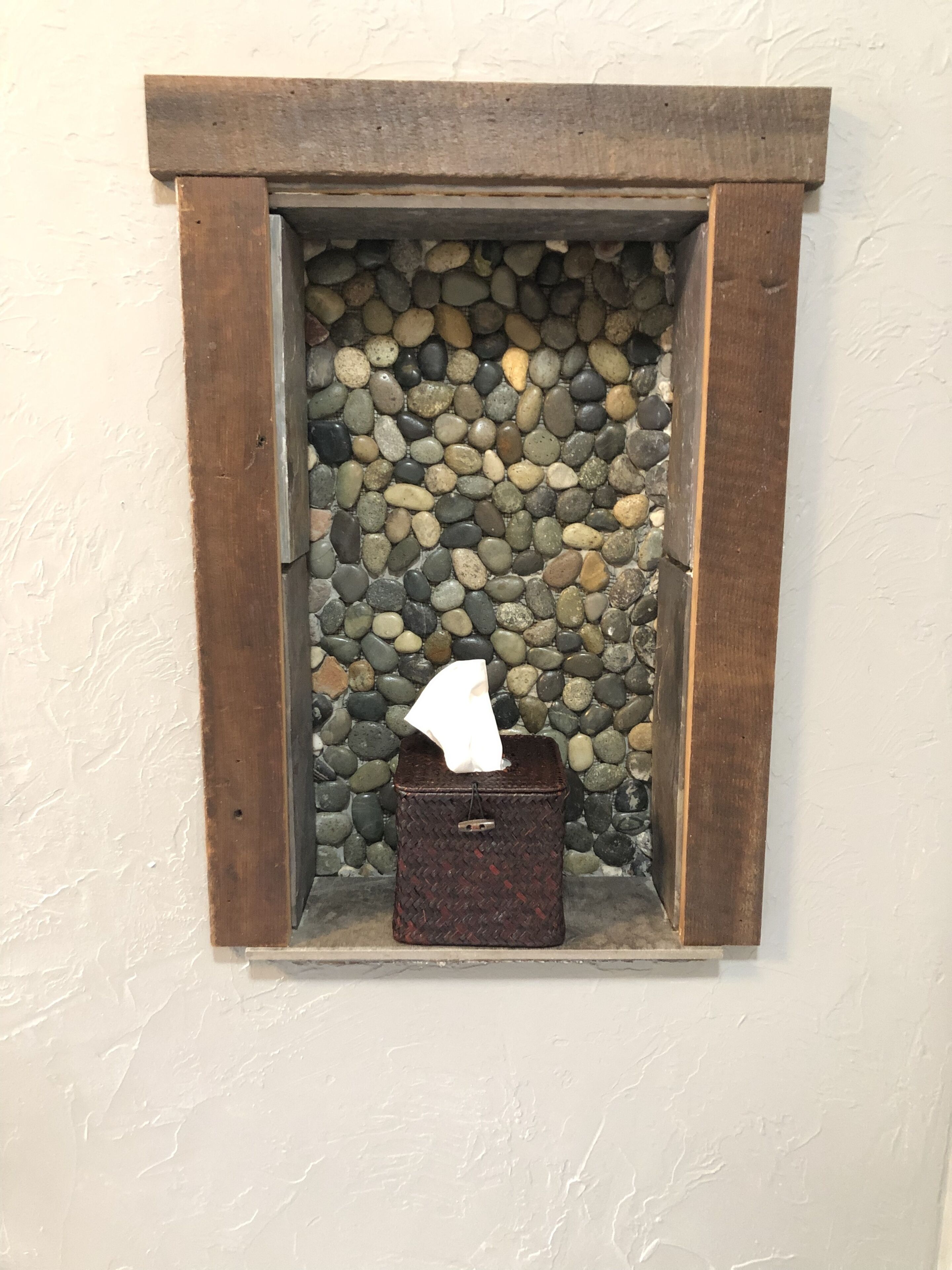 A small wooden box with a tissue box inside, placed in a niche with a stone wall background.