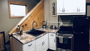 Cocina con armarios blancos, encimera de granito, refrigerador negro, estufa y ventana con vista a árboles.