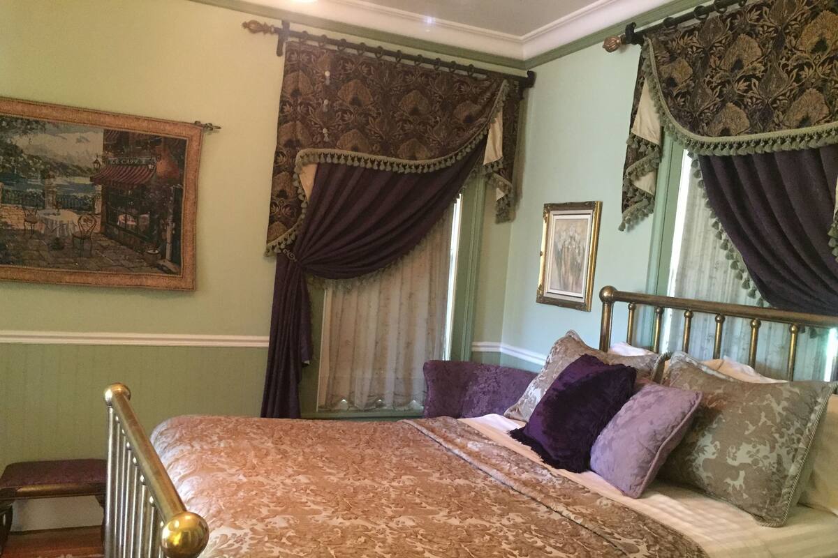 Een slaapkamer met een bed, gordijnen, een schilderij en een raam.