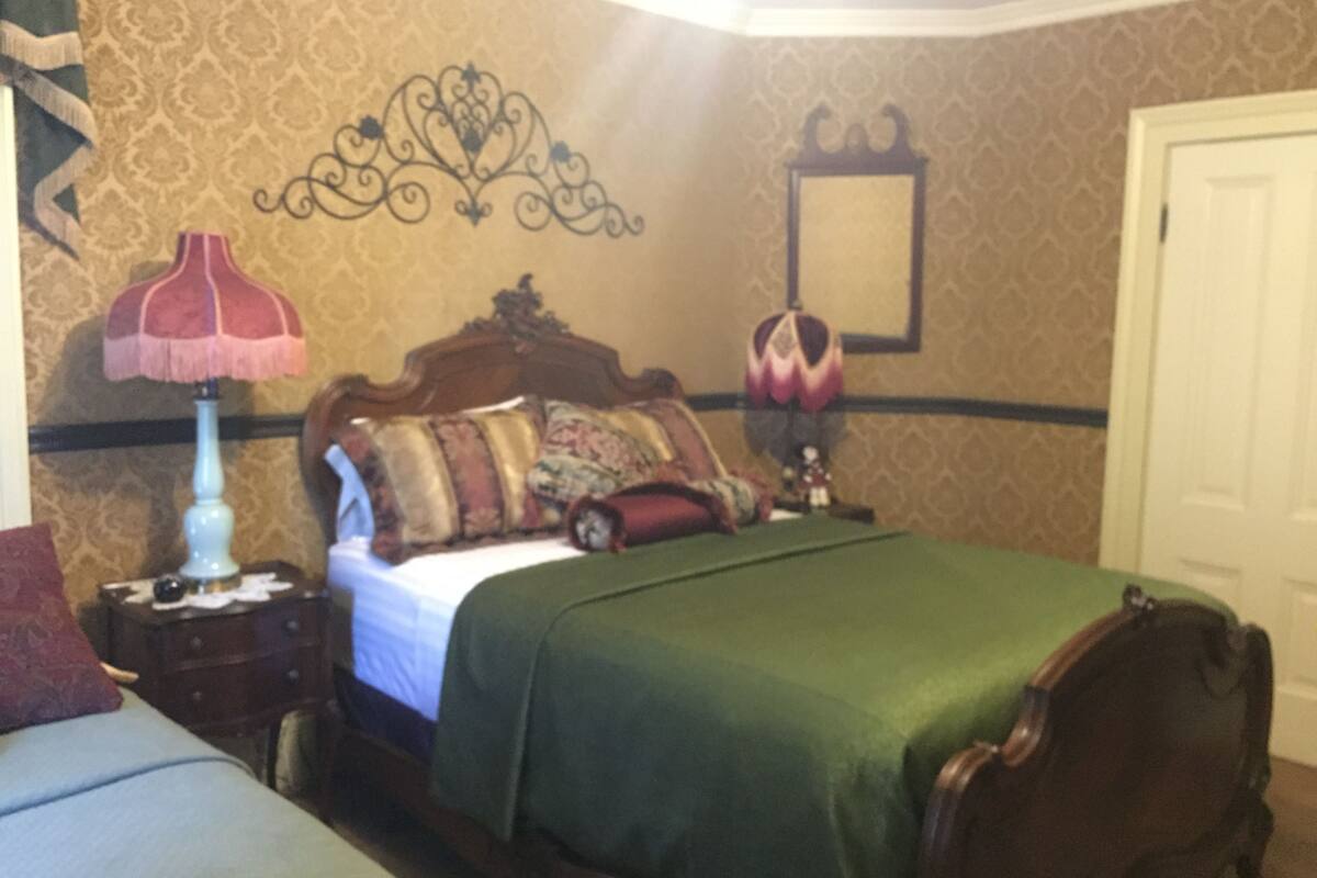 Een slaapkamer met een bed, nachtkastje, lamp en een spiegel aan de muur.