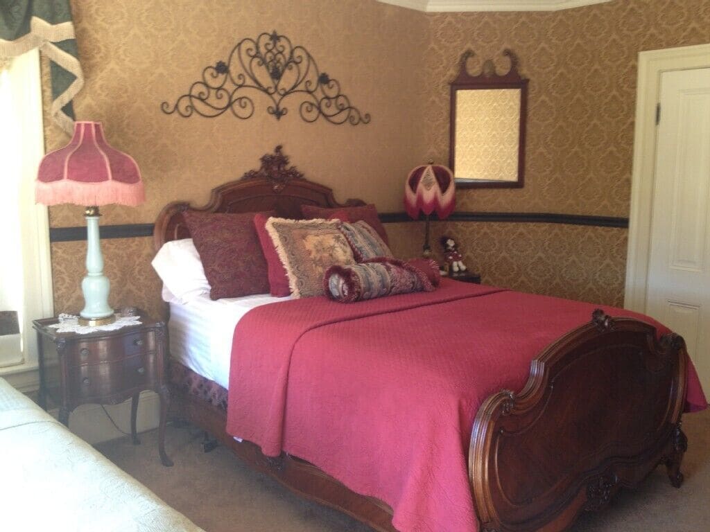 Un dormitorio con una cama de madera, una colcha roja, una mesita de noche con una lámpara y un adorno en la pared.