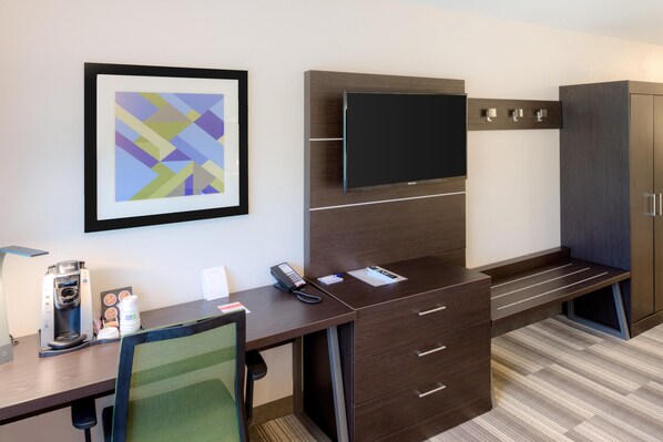Quarto de hotel moderno com escrivaninha, cadeira, TV de tela plana e uma pintura abstrata emoldurada.