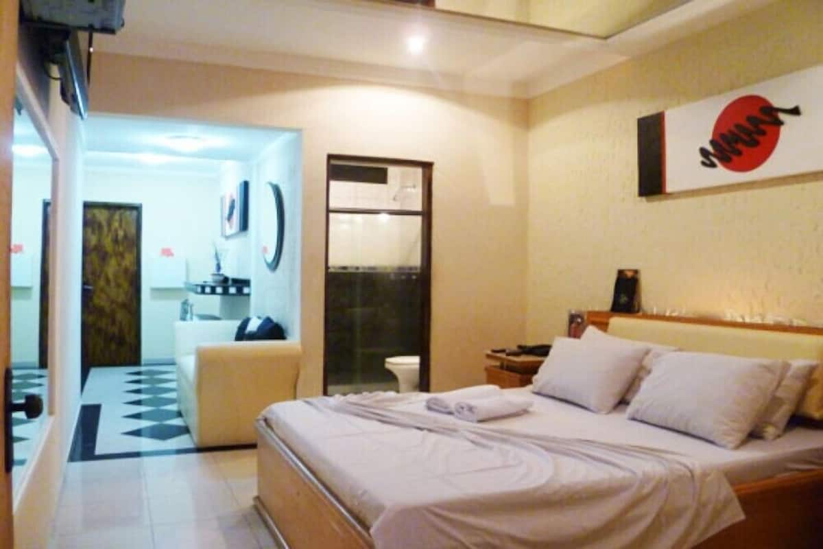 A hotel room with a bed, a small table, a chair, and a bathroom visible through an open door.
