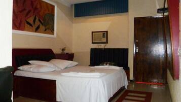 Quarto de hotel com cama de casal, uma mesinha, um quadro na parede e uma porta de madeira.