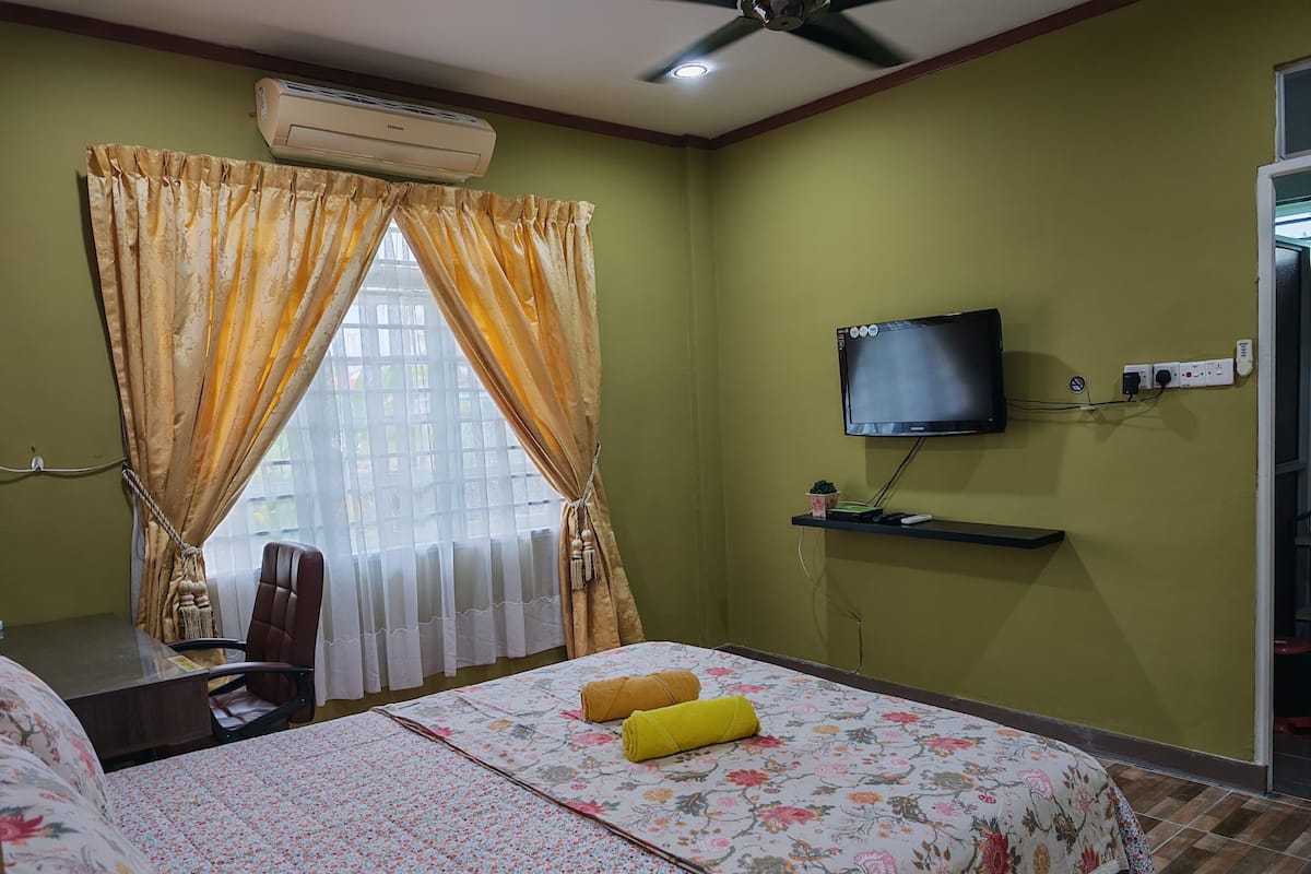 A hotel room with a bed, a desk, a chair, a TV, and an air conditioning unit.
