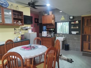 Una cocina con una mesa de comedor, sillas, armarios, un dispensador de agua y un perro pequeño en el suelo.