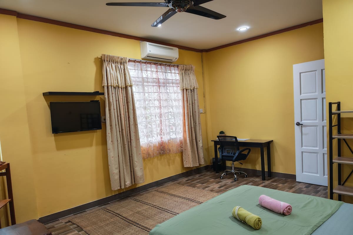 A room with a bed, a desk, a chair, a television, an air conditioner, and a door.