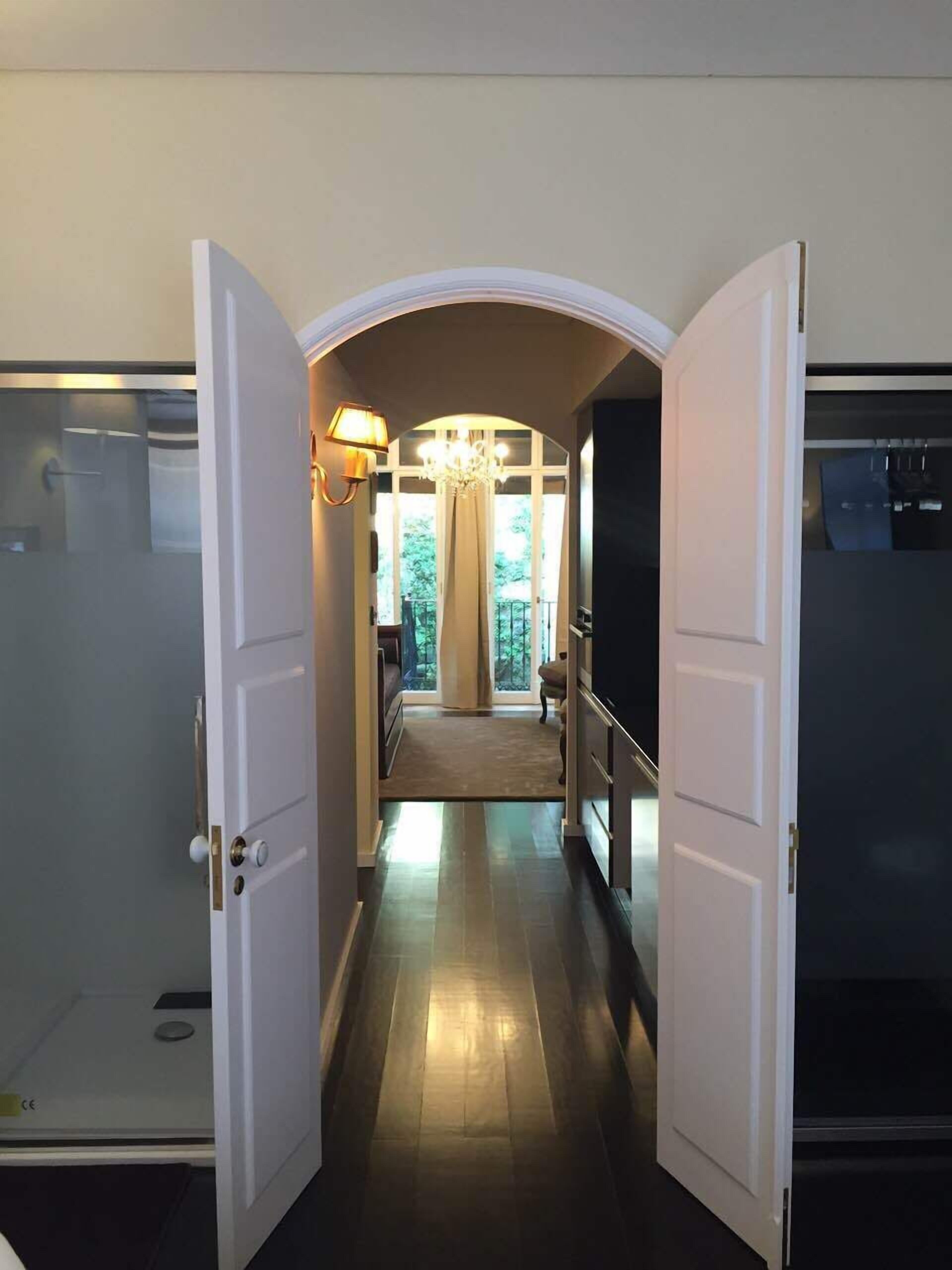 A hallway with a chandelier, a view to a balcony, and a door leading to a room with a large window.