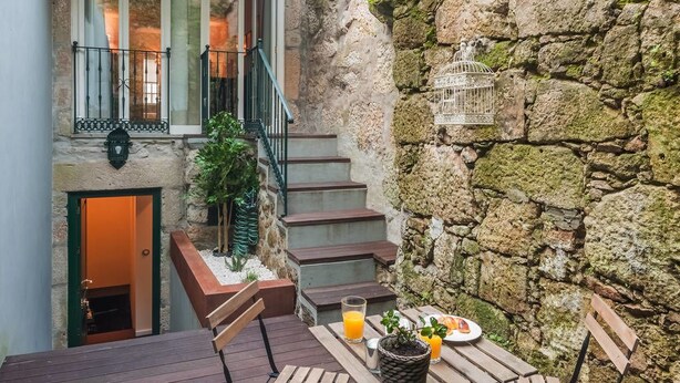 A stone wall with a birdcage, a staircase, and a table with a drink and fruit. - DuCarmo Apartments Caves Vinho do Porto (Vila Nova de Gaia)