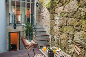 A stone wall with a birdcage, a staircase, and a table with a drink and fruit. - DuCarmo Apartments Caves Vinho do Porto (Vila Nova de Gaia)