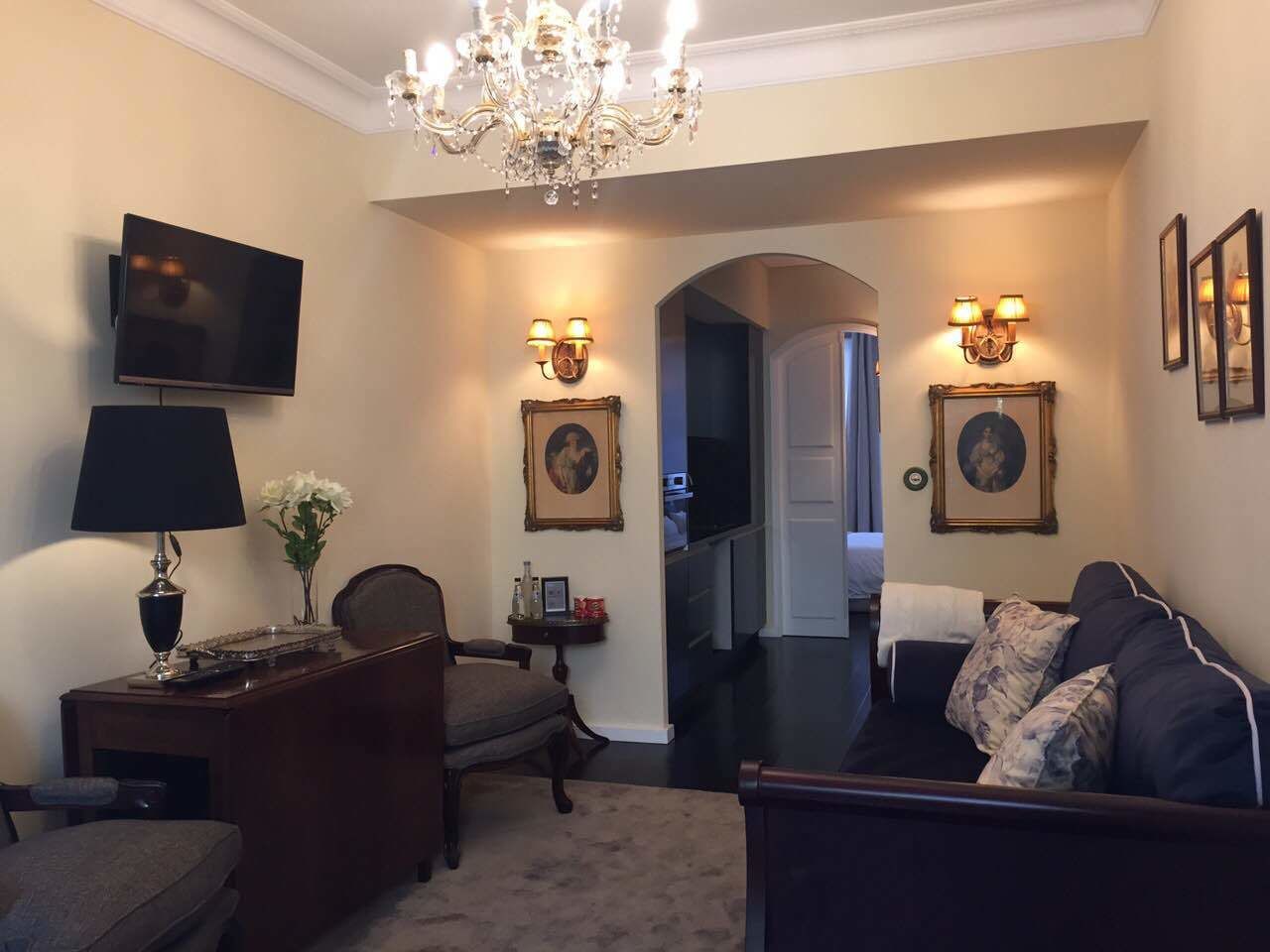 Un salon comprenant un téléviseur, un bureau, une chaise, un canapé et un lustre.