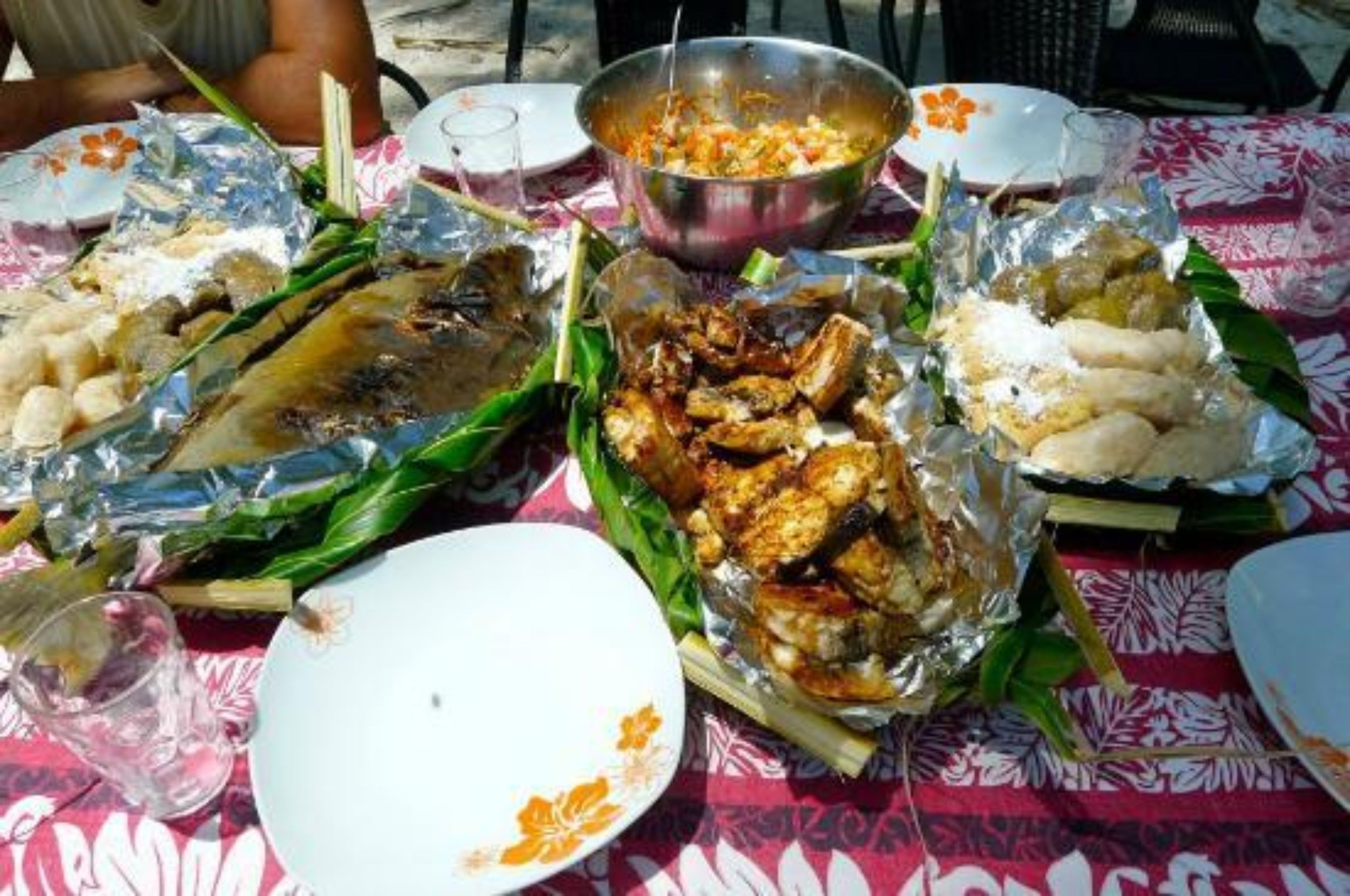 A table set with various dishes wrapped in leaves, a metal bowl, and a few plates.