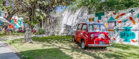 Un coche antiguo rojo estacionado en un jardín, con un mural de fondo.
