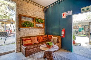 Un rincón acogedor con un sofá de cuero marrón, una mesa redonda de madera y una pared de ladrillo con estantería de plantas verdes.