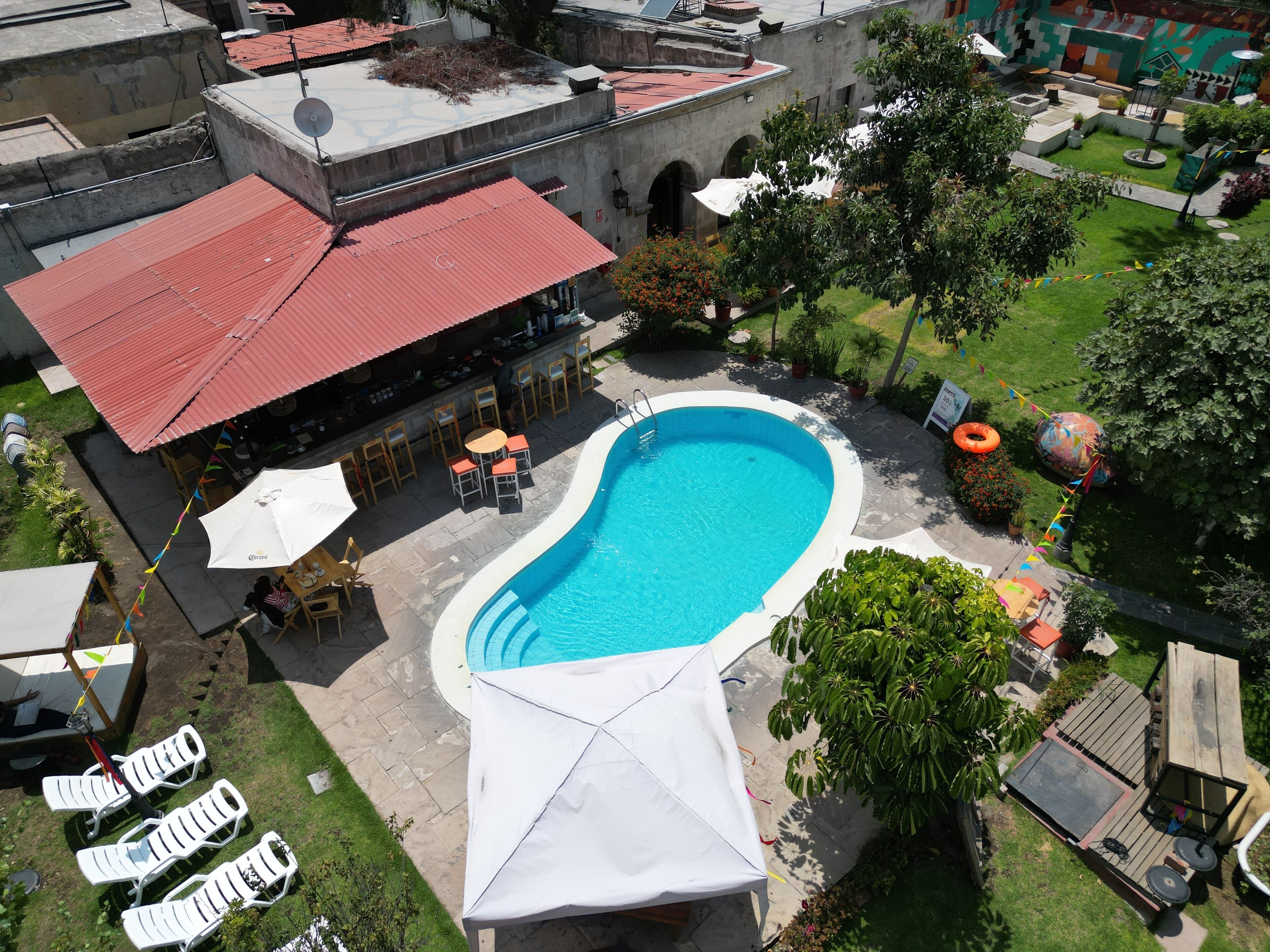 A swimming pool with lounge chairs and umbrellas, surrounded by greenery and a building with a red roof.