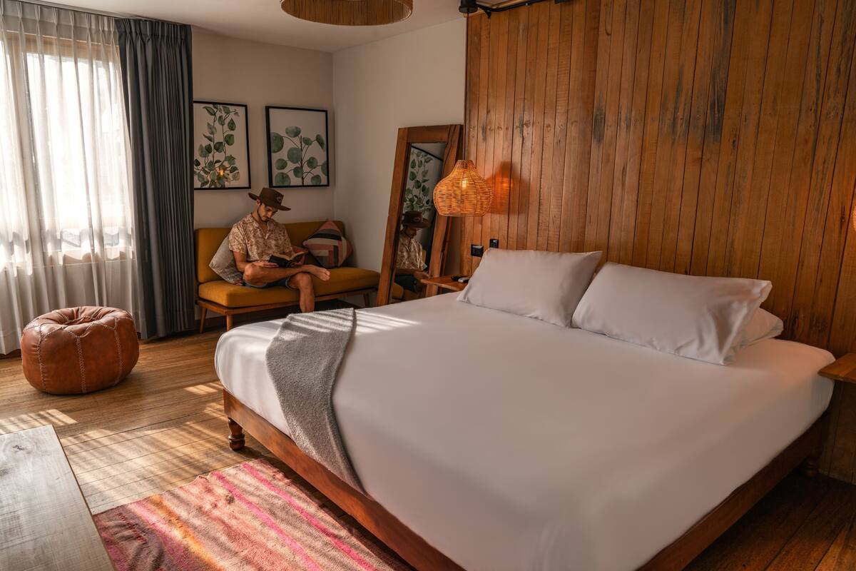 Un dormitorio con una cama grande, paredes de madera, un espejo y una ventana con cortinas.