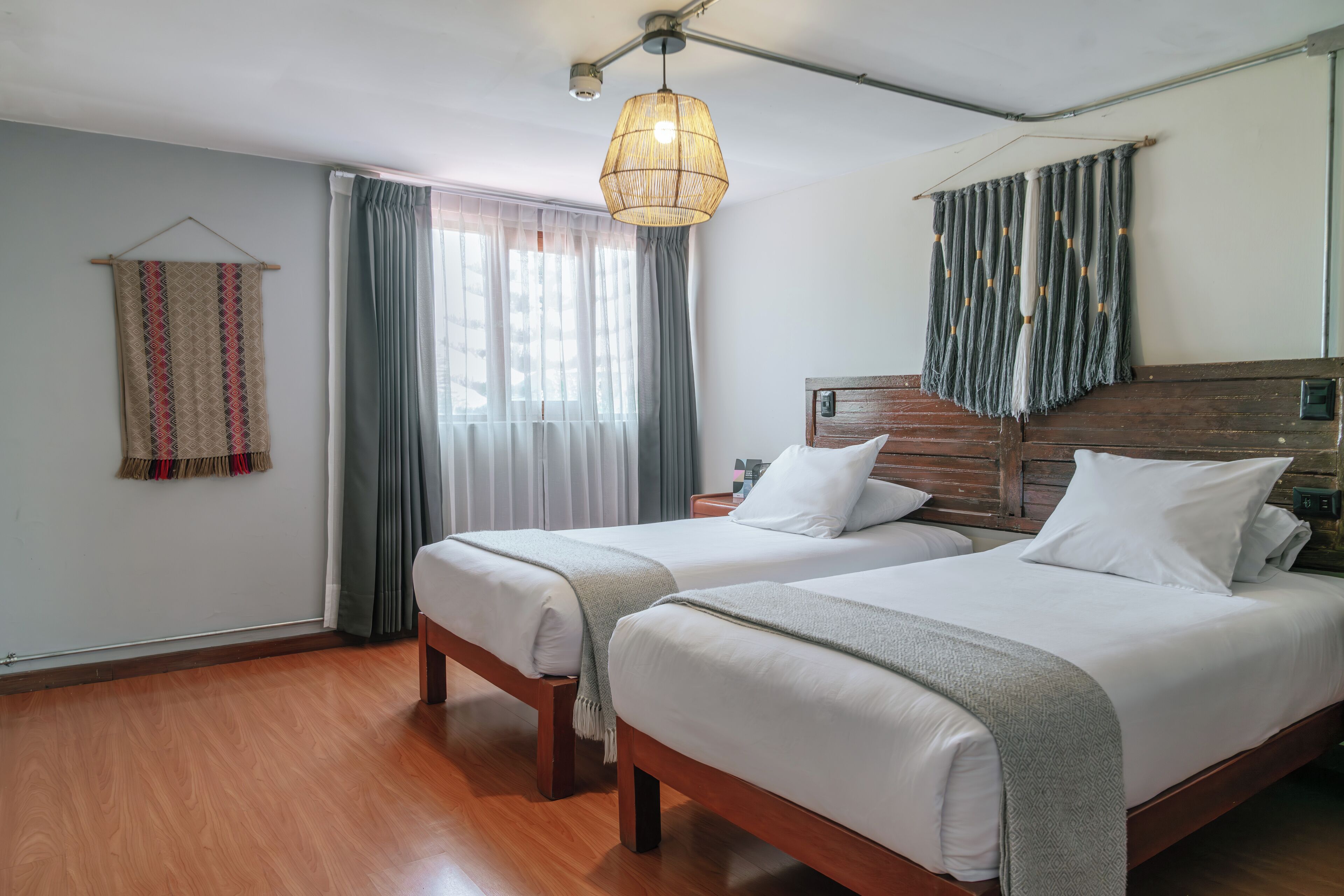 Une chambre d’hôtel avec deux lits, un plancher en bois, un luminaire suspendu et une fenêtre avec des rideaux.