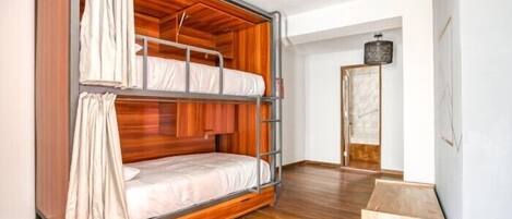 A bunk bed with a wooden frame and metal ladder, a wooden floor, and a white door in the background.