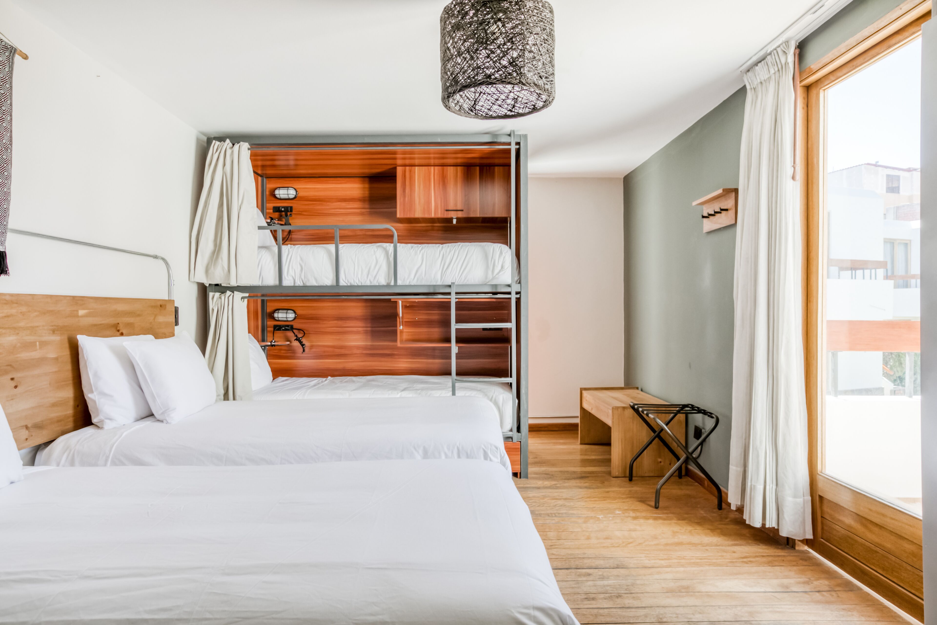 Habitación con literas, cabecera de madera, una mesita pequeña y una lámpara colgante.