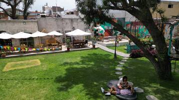 Un espacio al aire libre con césped, asientos, sombrillas, un mural y un árbol.