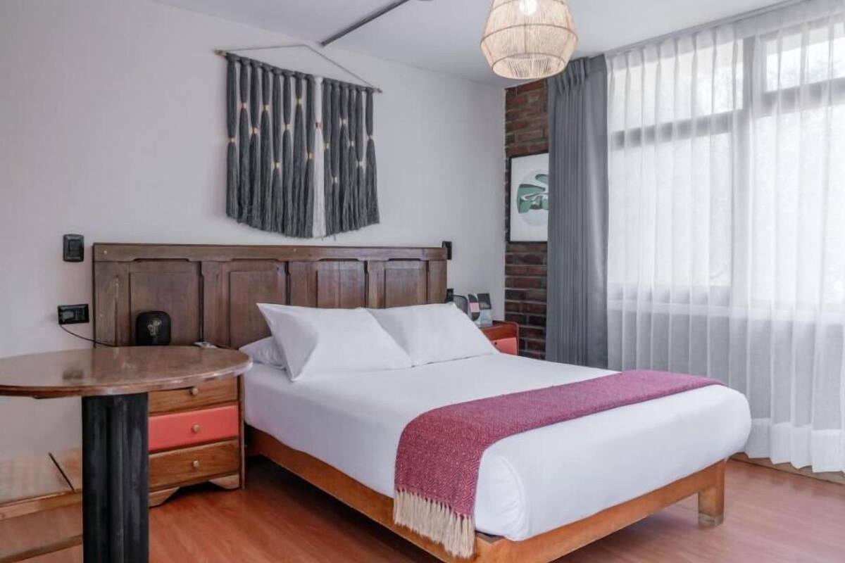 Un dormitorio ordenado con una cama de madera, una mesita de noche y una lámpara colgante.