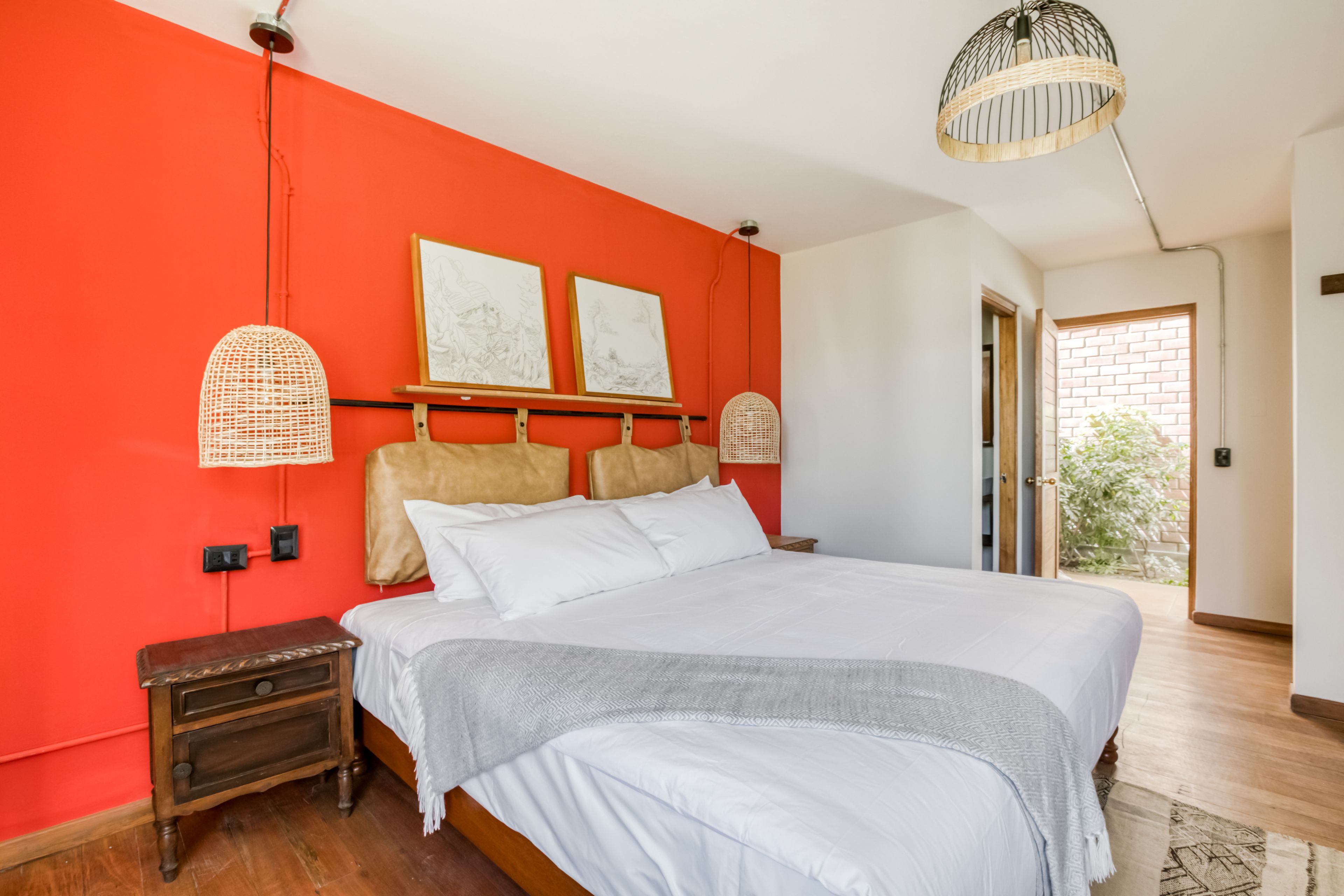 Un dormitorio con una cama grande, una pared roja, dos cuadros enmarcados y una mesita de noche de madera.