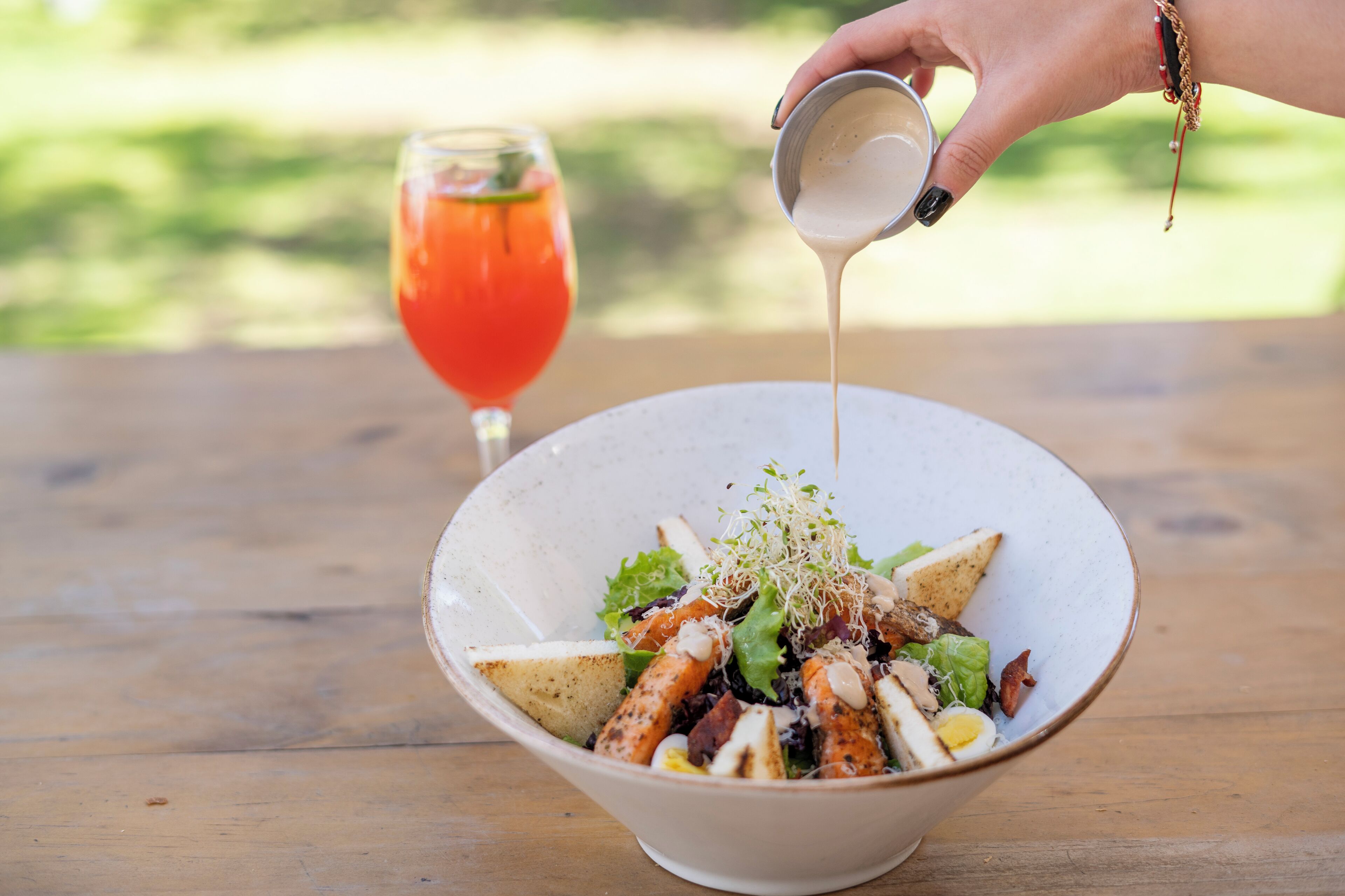A bowl of salad with various ingredients being poured from a small container.