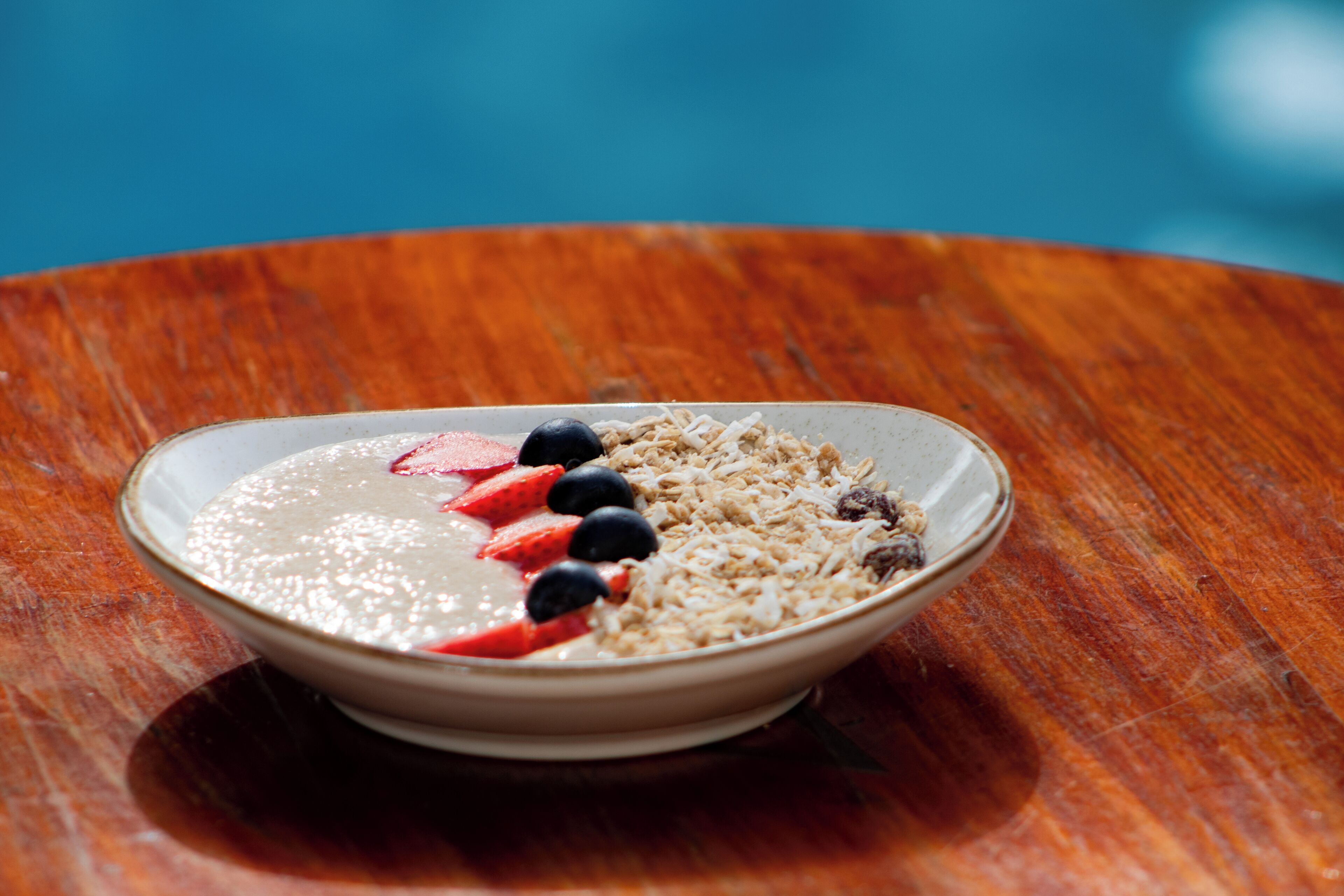 A bowl of cereal with strawberries and blueberries on a wooden table.