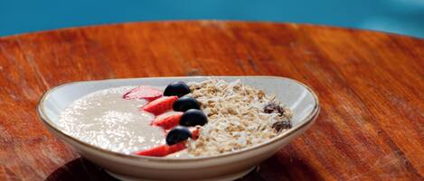 A bowl of cereal with strawberries and blueberries on a wooden table.