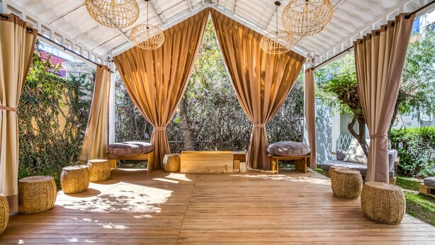 A covered outdoor seating area with wooden flooring, woven poufs, and a bench. - qema Arequipa (Arequipa)