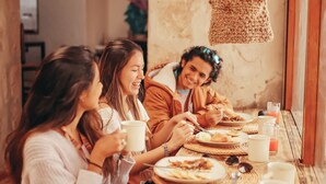 A group of people dining at a wooden table with woven placemats, surrounded by rustic stone walls and a hanging light fixture. - qema Arequipa (Arequipa)