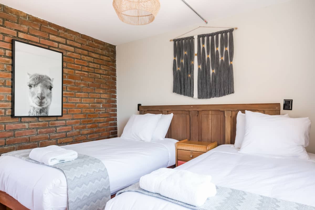 Habitación de hotel con dos camas, una pared de ladrillo, cabecero de madera y un cuadro enmarcado en la pared.