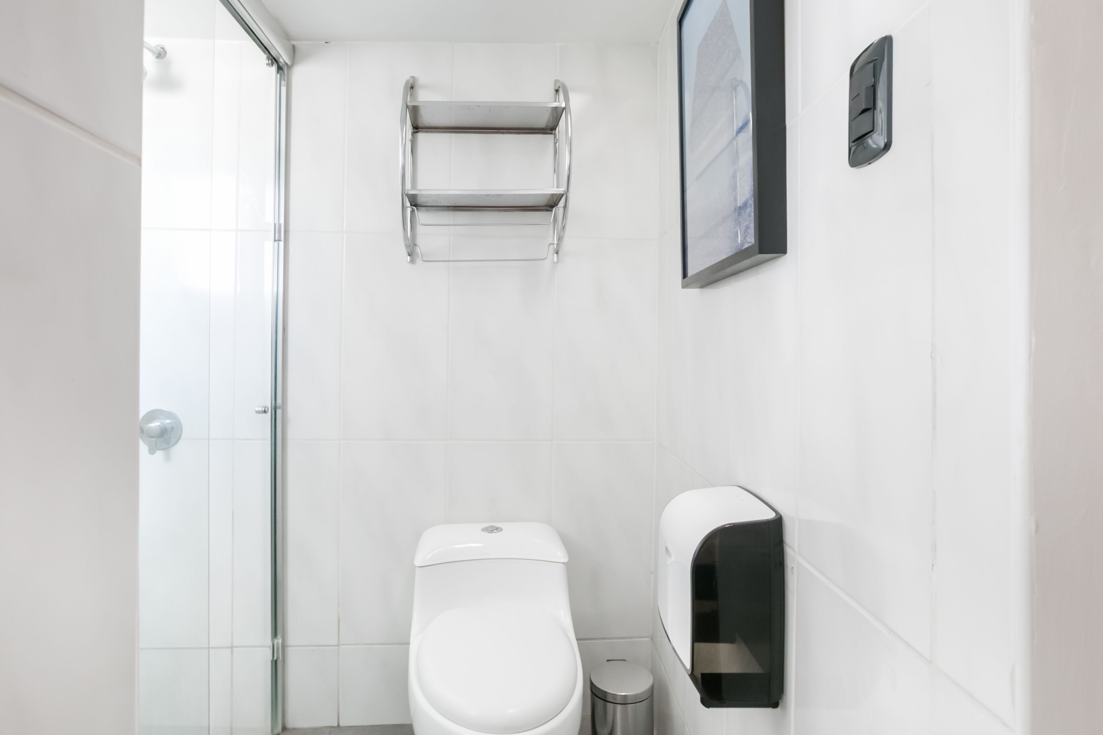 Um banheiro pequeno e moderno, com vaso sanitário, lixeira, porta-toalhas e dispensador de sabonete.