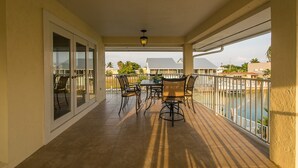A covered balcony with a table and chairs, a view of the water, and a building in the background. - Salty Anglers: Waterfront Heated Pool, Dock & Walk to Sombrero Beach in Marathon (Marathon)